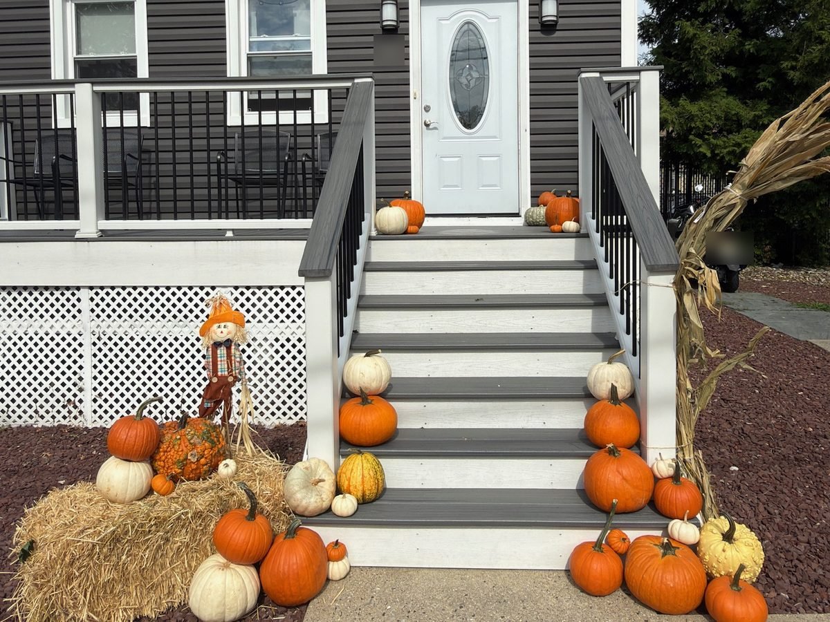 Real Doorstep package porch in Hackensack NJ styled by Pascack Porches with a straw bale, scarecrow, cornstalks, and pumpkins lining both sides of the steps