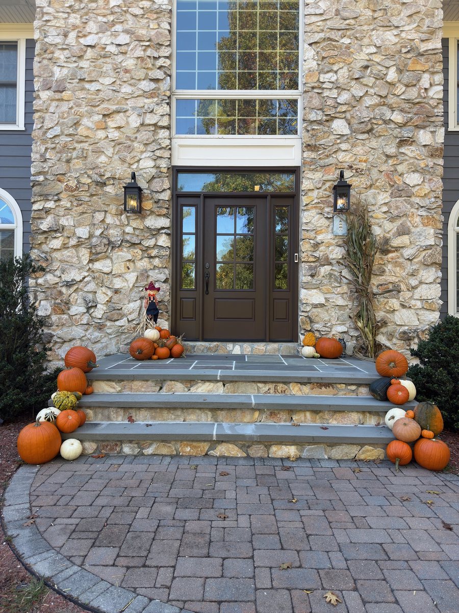 Pumpkin porch display lining stone front steps in Bergen County, NJ, with a scarecrow and cornstalks by the door