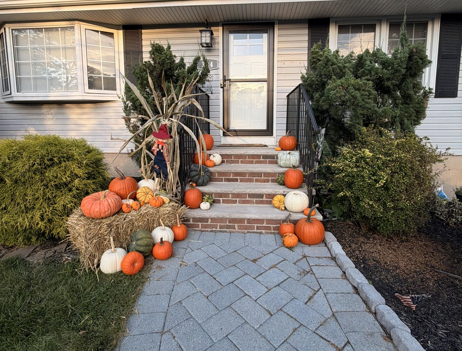 Real fall porch pumpkin display styled by Pascack Porches in Hillsdale NJ, with straw bales, cornstalks, and a scarecrow