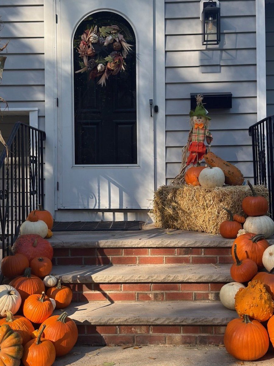 The same porch after: pumpkins pouring down both sides of the steps, a straw bale, a scarecrow, and cornstalks