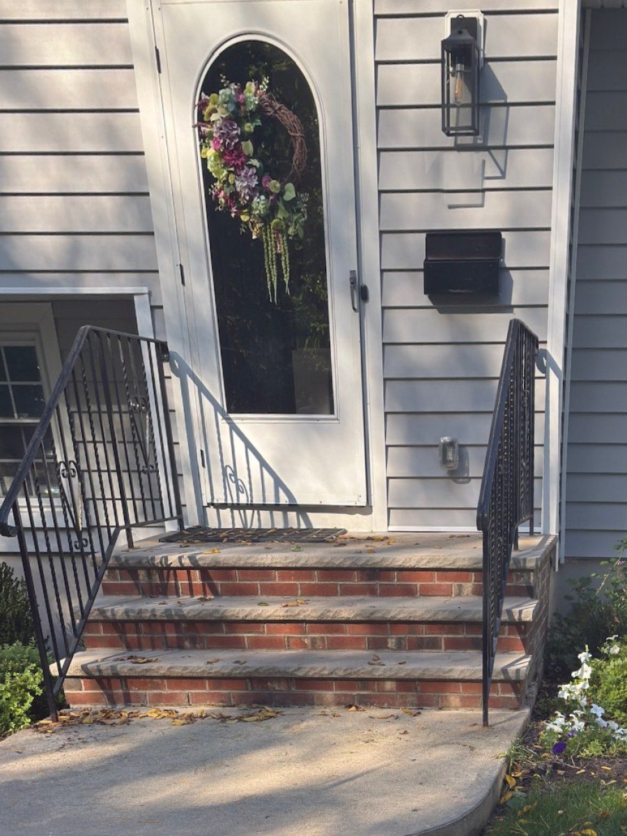 The porch before: bare brick steps and black railings by a white front door